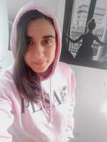 Selfie of Pili from above and smiling directly into the camera. She has long dark wavy hear and wears a pinky hoodie with black words in the front.
